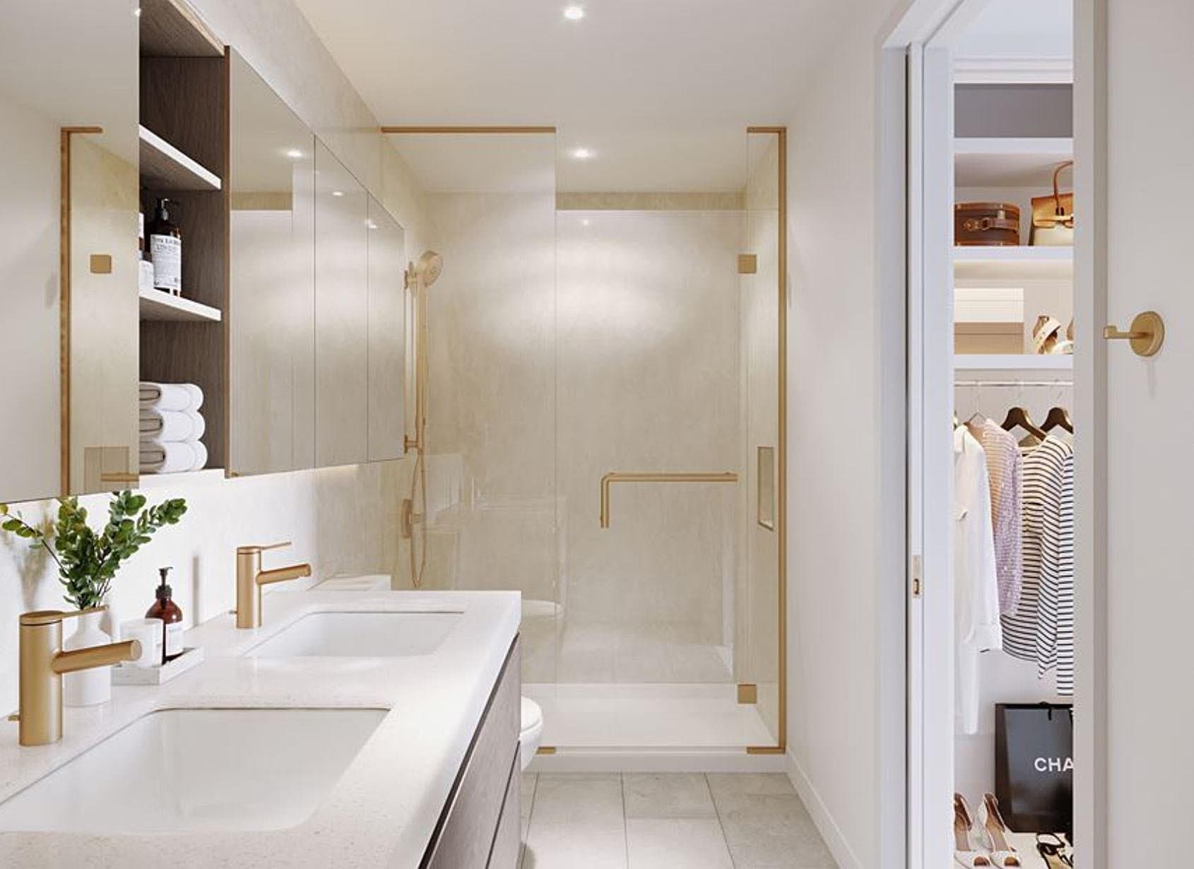 Central Park House – A modern ensuite bathroom featuring a double vanity with brushed gold faucets, mirrored medicine cabinets, and a glass-enclosed walk-in shower with matching gold trim. An open sliding doorway on the right reveals an organized walk-in closet with clothes on hangers and neatly displayed accessories.
