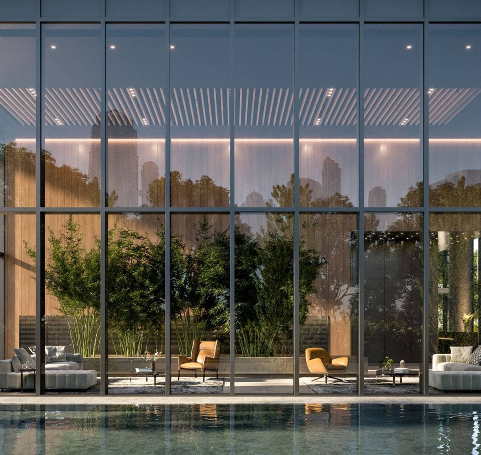 Central Park House – A view across an outdoor swimming pool looking through floor-to-ceiling glass walls into a double-height lounge area furnished with armchairs and sofas. Warm wood panelling, indoor bamboo plants, and recessed lighting create a sophisticated, calm atmosphere inside, with reflections of city skyscrapers visible on the glass.