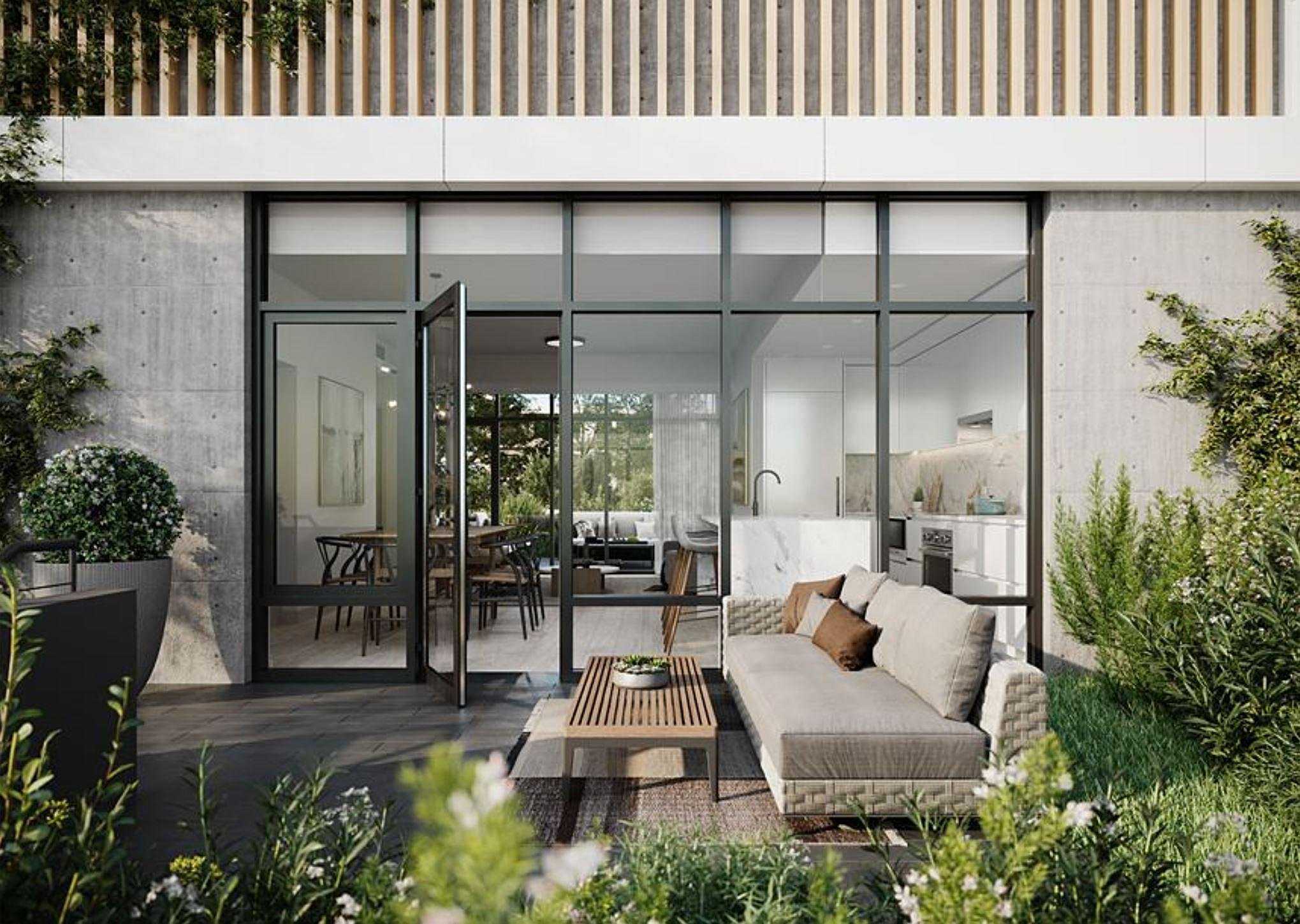 Central Park House – A private ground-floor patio features a woven outdoor sofa and slatted wooden coffee table surrounded by lush green foliage and board-formed concrete walls. Large black-framed glass doors open directly into a modern open-concept kitchen and dining area bathed in natural daylight.