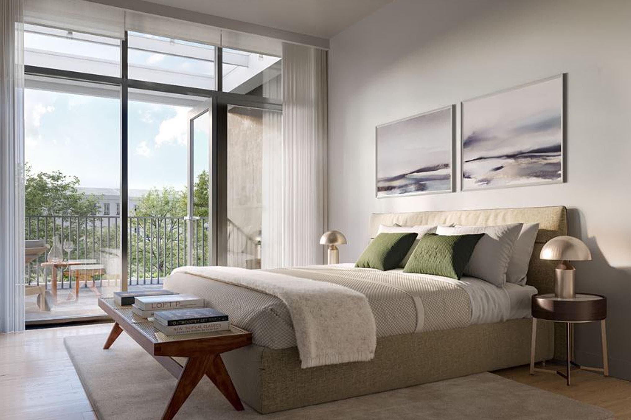 Central Park House – A modern, sunlit bedroom featuring a neatly dressed bed with green accent pillows, warm bedside lamps, and a bench at the foot of the bed. Large floor-to-ceiling glass patio doors open onto a private balcony overlooking lush green trees.
