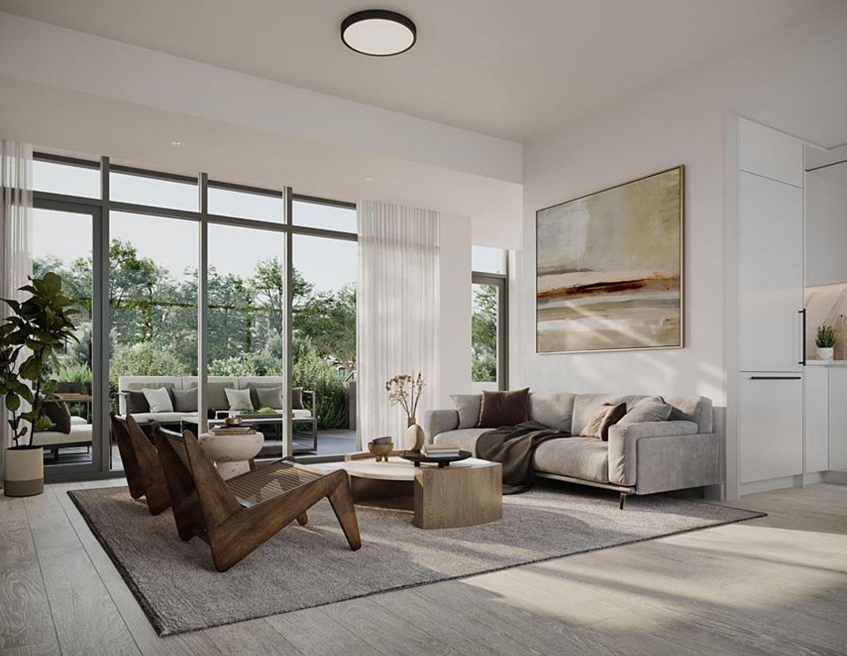 Central Park House – A modern bright open-concept living room features a plush grey sofa, low wooden accent chairs, and neutral decor over light hardwood floors. Wall-to-wall glass patio doors open onto a private outdoor terrace surrounded by lush green trees in soft daylight.