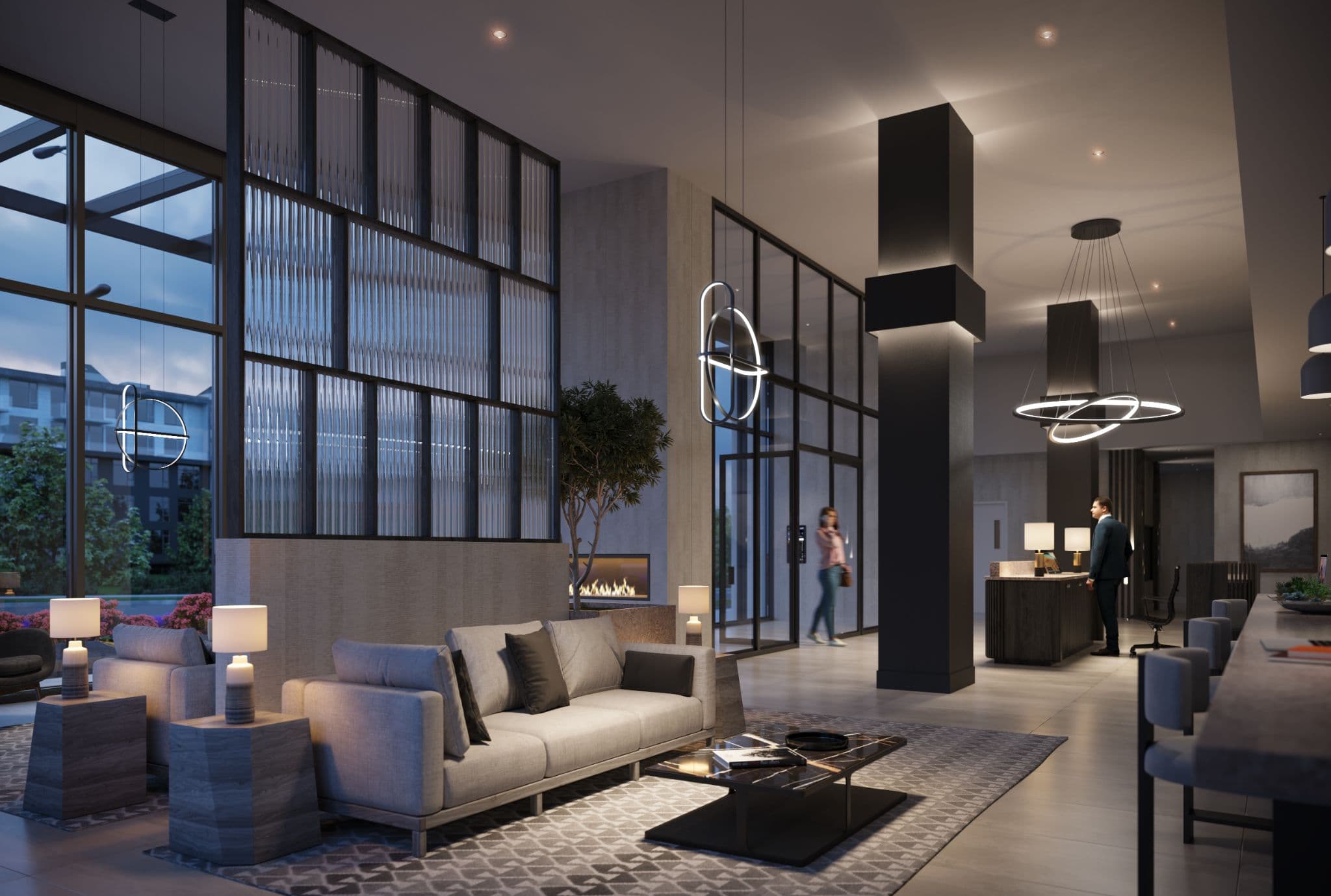 Vue – A high-ceiling contemporary building lobby and lounge area at twilight, featuring modern sofas, a marble coffee table, a glass partition, and an indoor fireplace. Warmly lit with sculptural halo pendant lights, the space includes a concierge reception desk and expansive glass doors leading to the exterior.