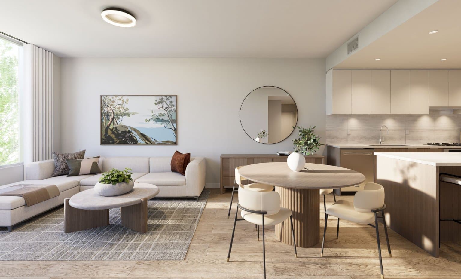 Goldfinch – Open-concept living, dining, and kitchen area with a grey sectional, round dining table, and light wood flooring.
