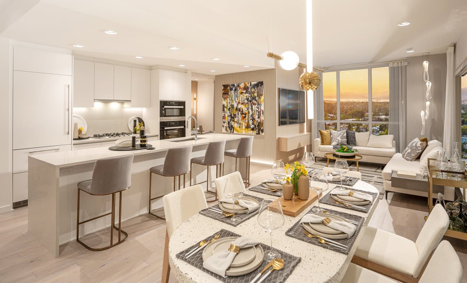 Claridge House – This open-concept interior showcases a fully set modern dining table leading into a sleek white kitchen with a spacious waterfall island and barstools. Large floor-to-ceiling windows in the adjacent living room frame an expansive view of distant water and mountains bathed in warm golden sunset light.