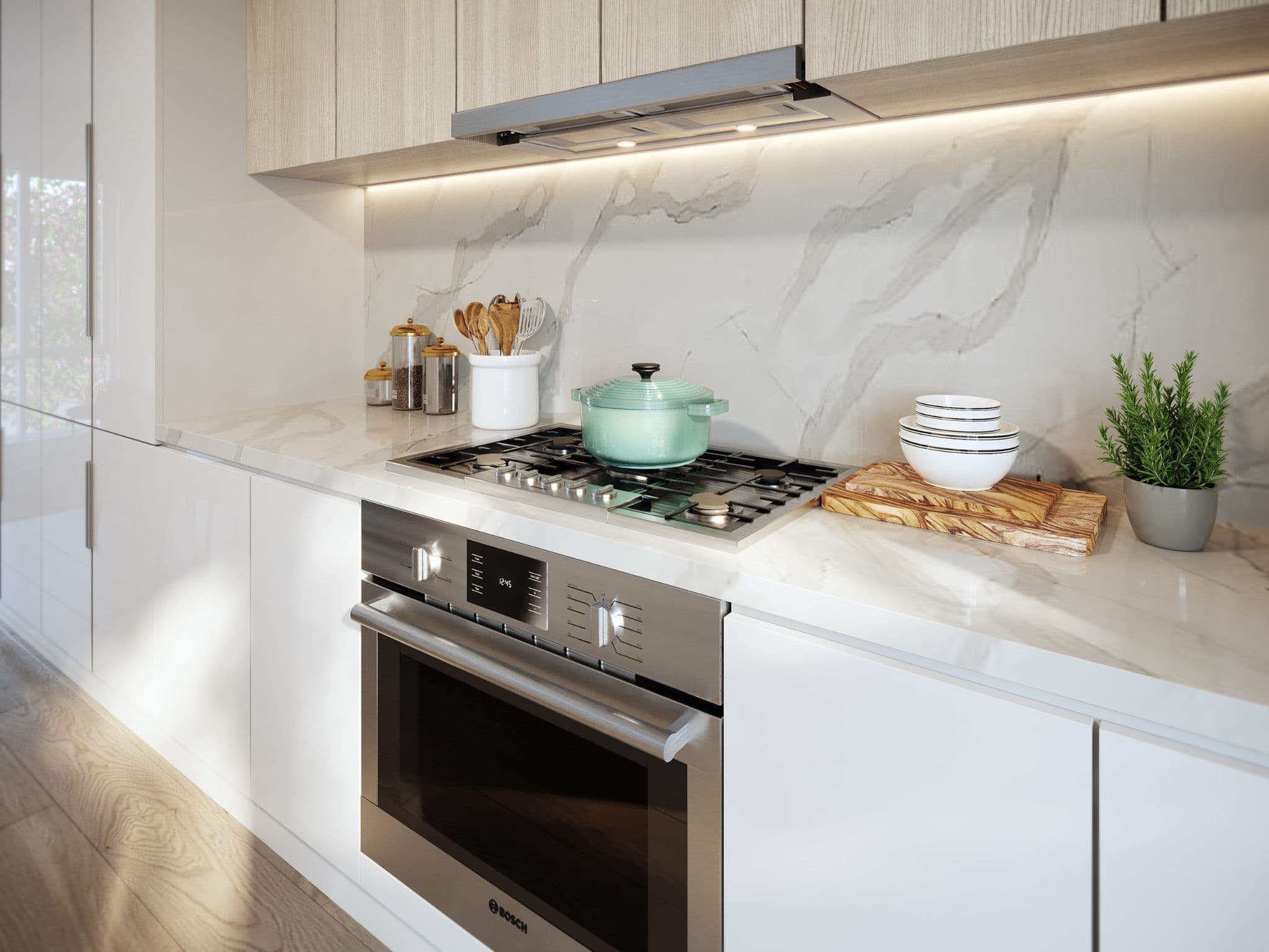West58 – A modern kitchen setup featuring a stainless-steel Bosch gas cooktop and built-in oven set against white marble-patterned countertops and a matching full-height backsplash. The space is detailed with light wood upper cabinets with under-cabinet lighting, sleek white lower cabinetry, and neat decorative accents including a mint green pot, stacked bowls, and a small potted plant.