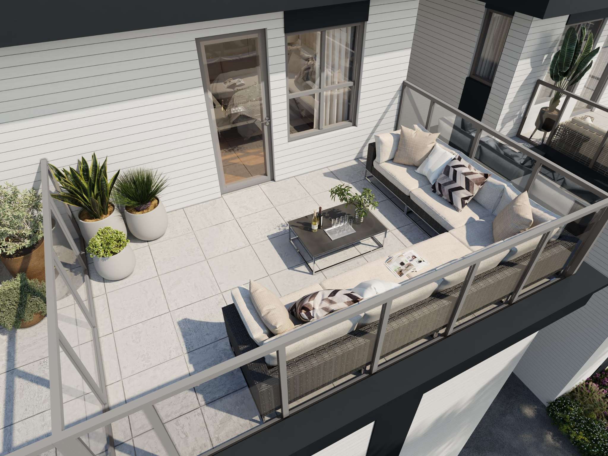 West58 – A spacious outdoor terrace balcony furnished with a large, grey wicker sectional sofa, patterned accent pillows, and a modern coffee table with drinks. Potted plants and white tiled flooring are enclosed by glass panel railings against the building's white horizontal siding on a bright, sunny day.