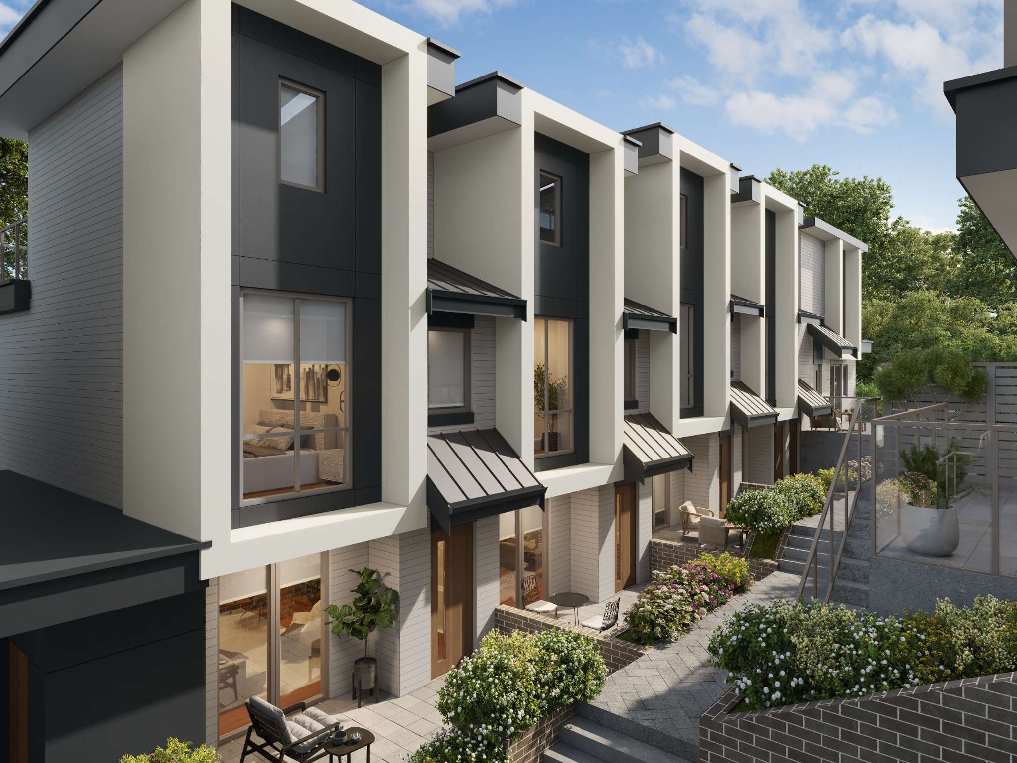 West58 – Exterior view of modern three-story townhomes featuring bold white box framing, dark grey paneling, and pitched door awnings. A stone-paved pedestrian walkway and stepped brick planters with lush greenery and flowers lead past the private ground-floor patios on a bright, clear day.
