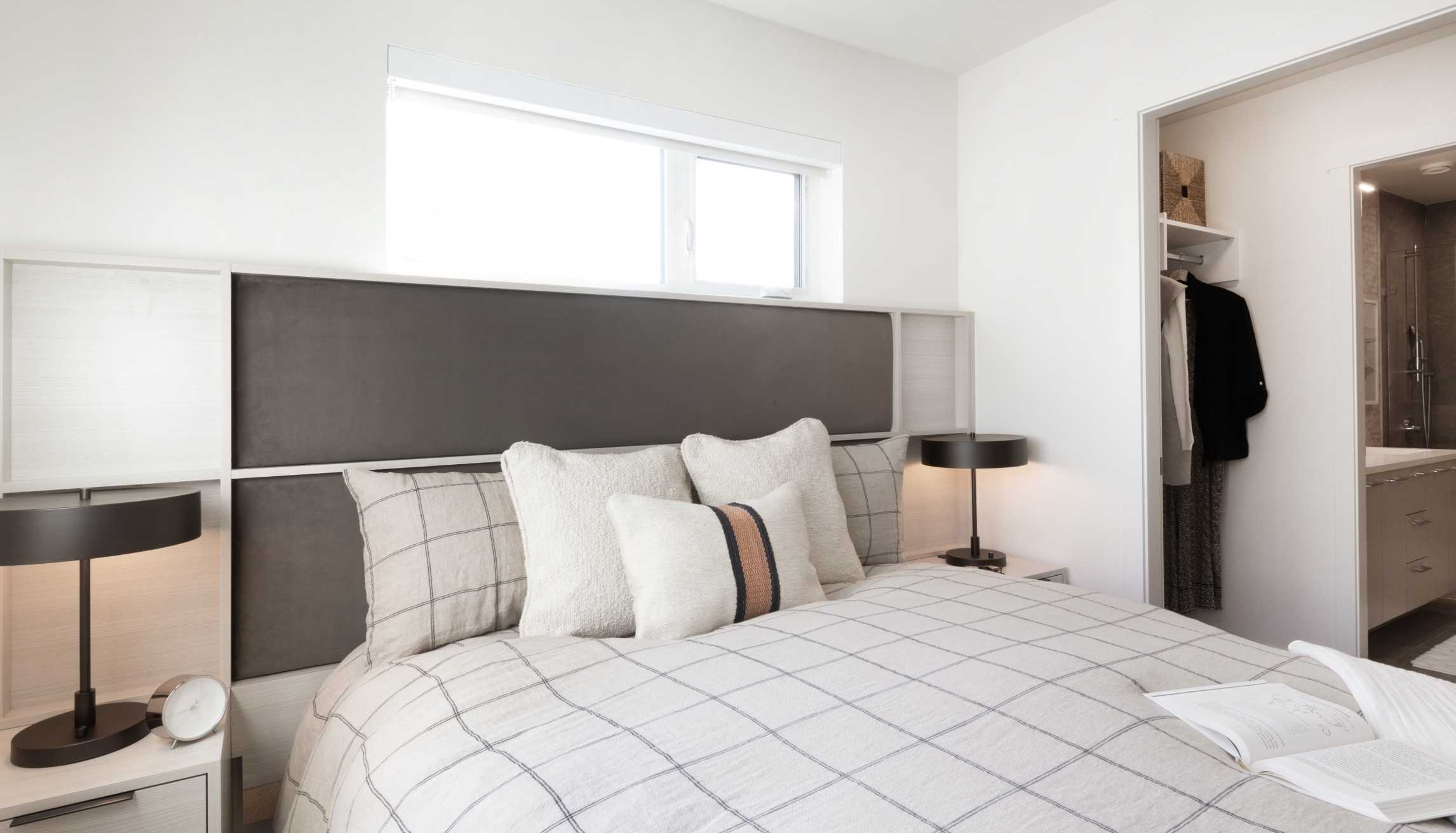 Cascadia – Bedroom with a dark upholstered headboard, bedside lamps, an open closet, and a glimpse of the ensuite bathroom.