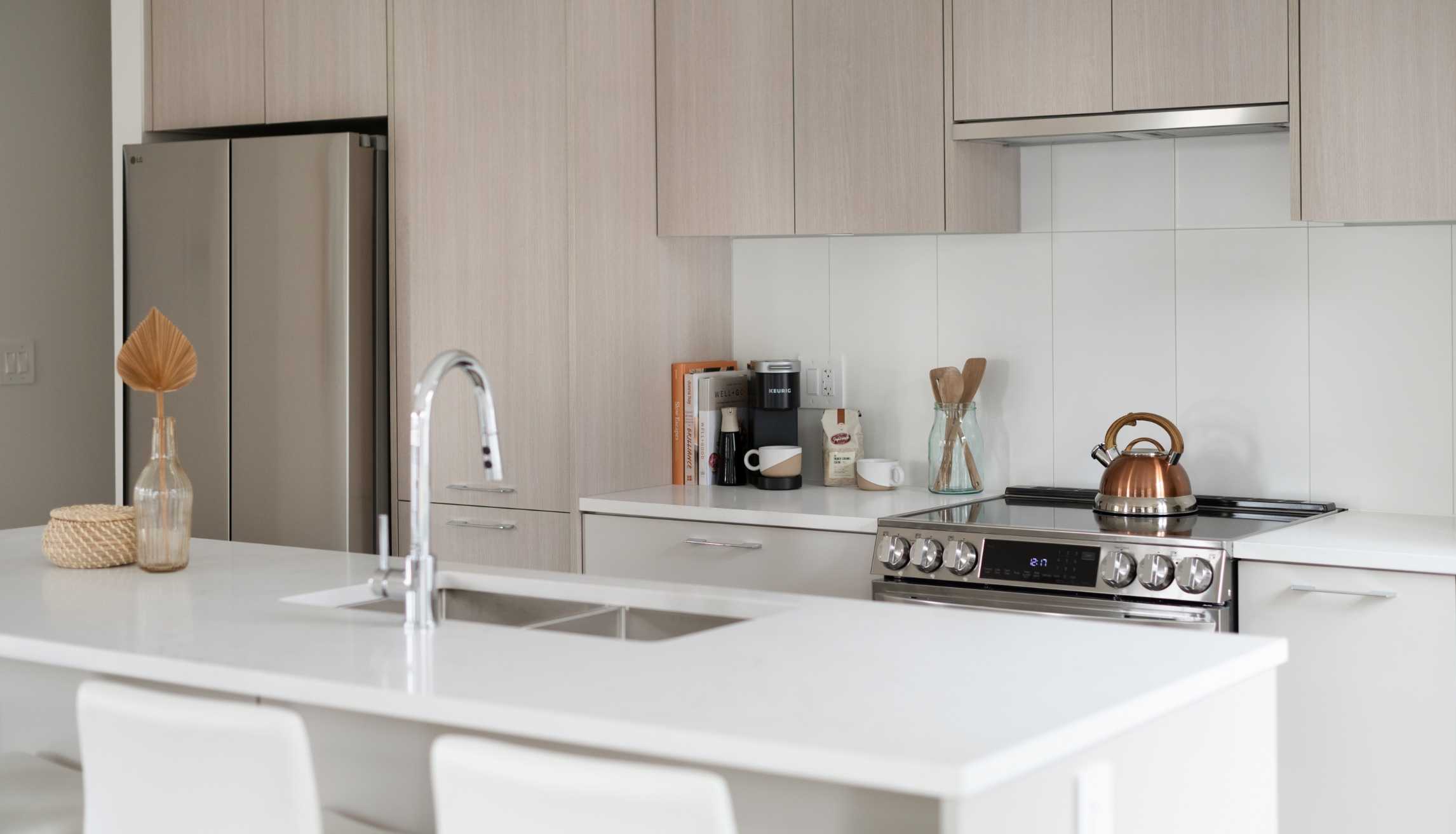 Cascadia – Close-up kitchen view showing a stainless steel fridge, gas range with copper kettle, and white quartz countertops.