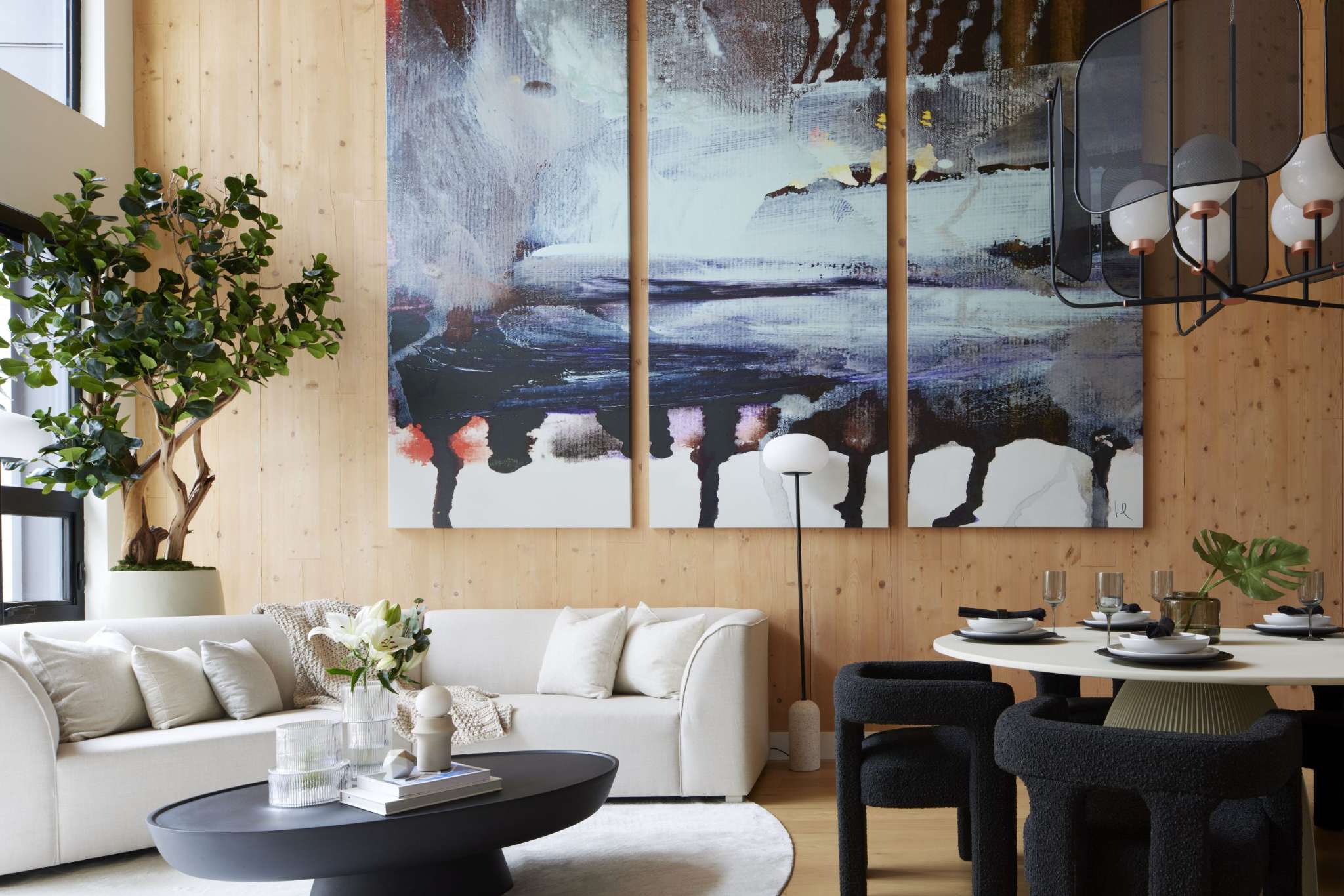 Timber House – Double-height living and dining space with an exposed mass-timber plank feature wall, large abstract triptych artwork, white sofa, black boucle dining chairs, and a sculptural black pendant light.