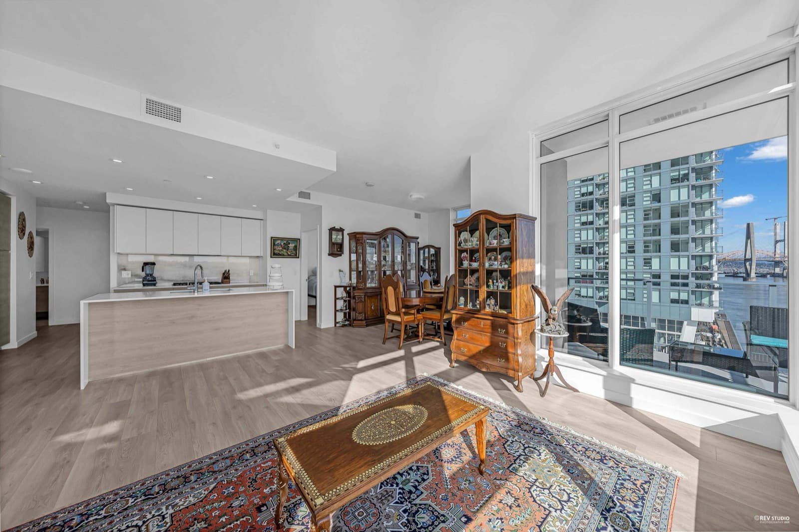 Pier West – Open-concept kitchen and dining area with antique furniture, floor-to-ceiling windows showing city high-rises and a bridge.