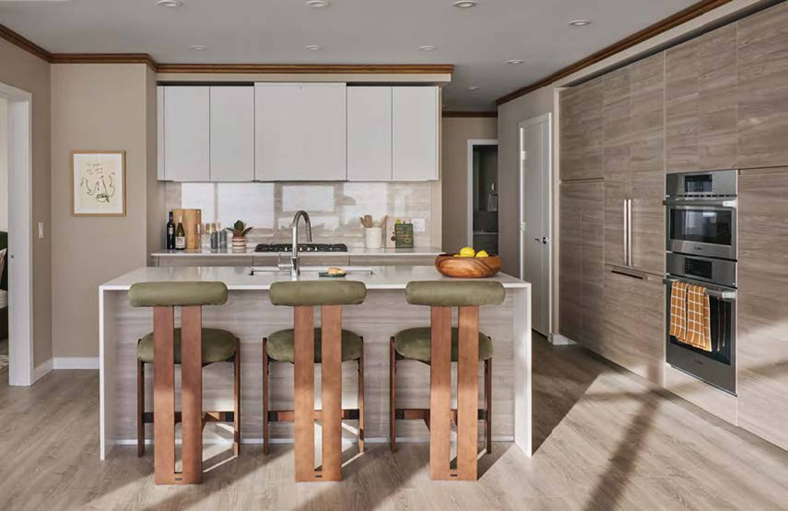Pier West – Kitchen with a wood-toned island, three green barstools, and built-in stainless steel wall ovens and refrigerator.