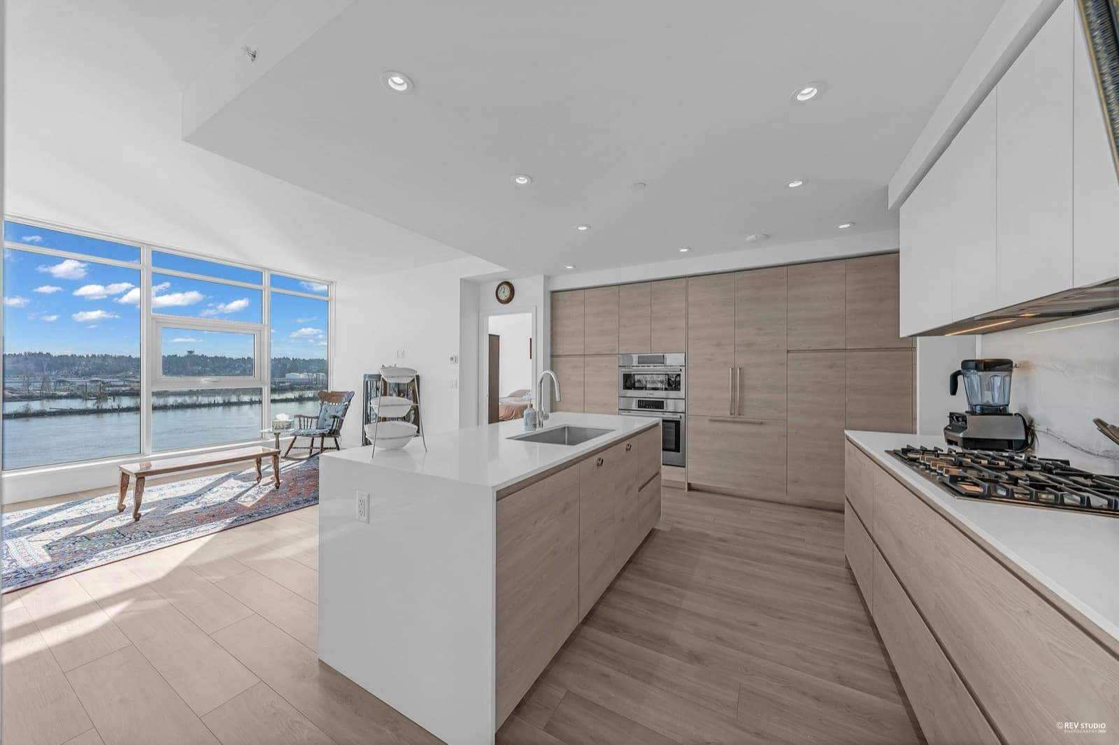 Pier West – Kitchen with a white island, light wood cabinetry, and a floor-to-ceiling window showing a river view.