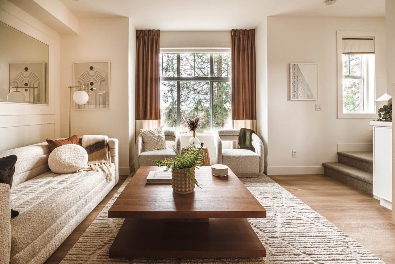 The Loop – Living room seating area with a cream sofa, two boucle accent chairs by a window, wood coffee table, and a staircase to the side.