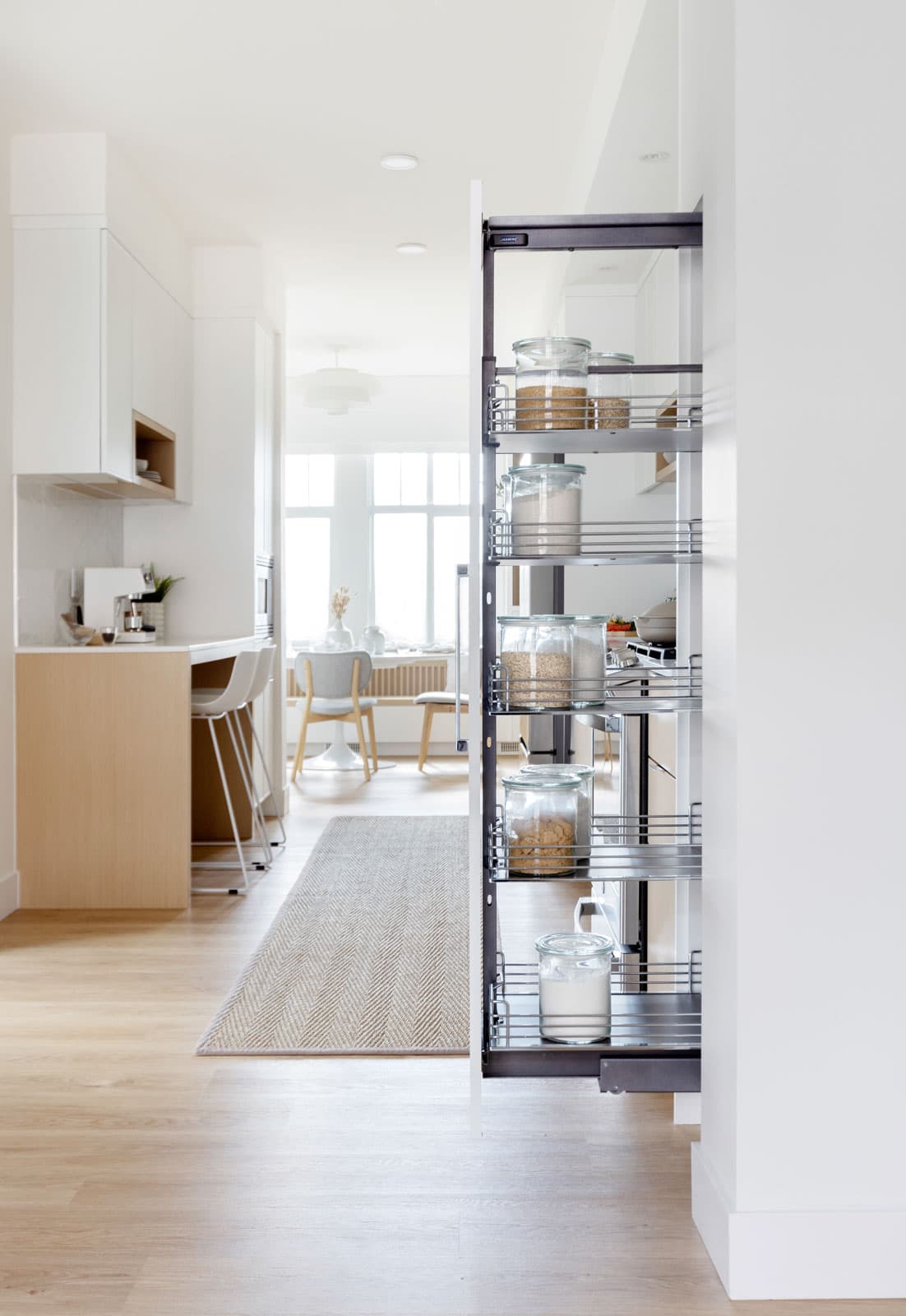 The Loop – Hallway with a pulled-out pantry organizer showing glass storage jars, leading to a bright kitchen and dining area beyond.