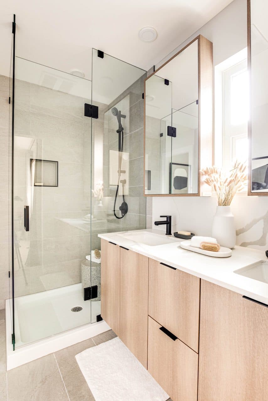 The Loop – Bathroom with a glass-enclosed shower, black fixtures, floating wood vanity with double mirrors, and a dried floral arrangement.