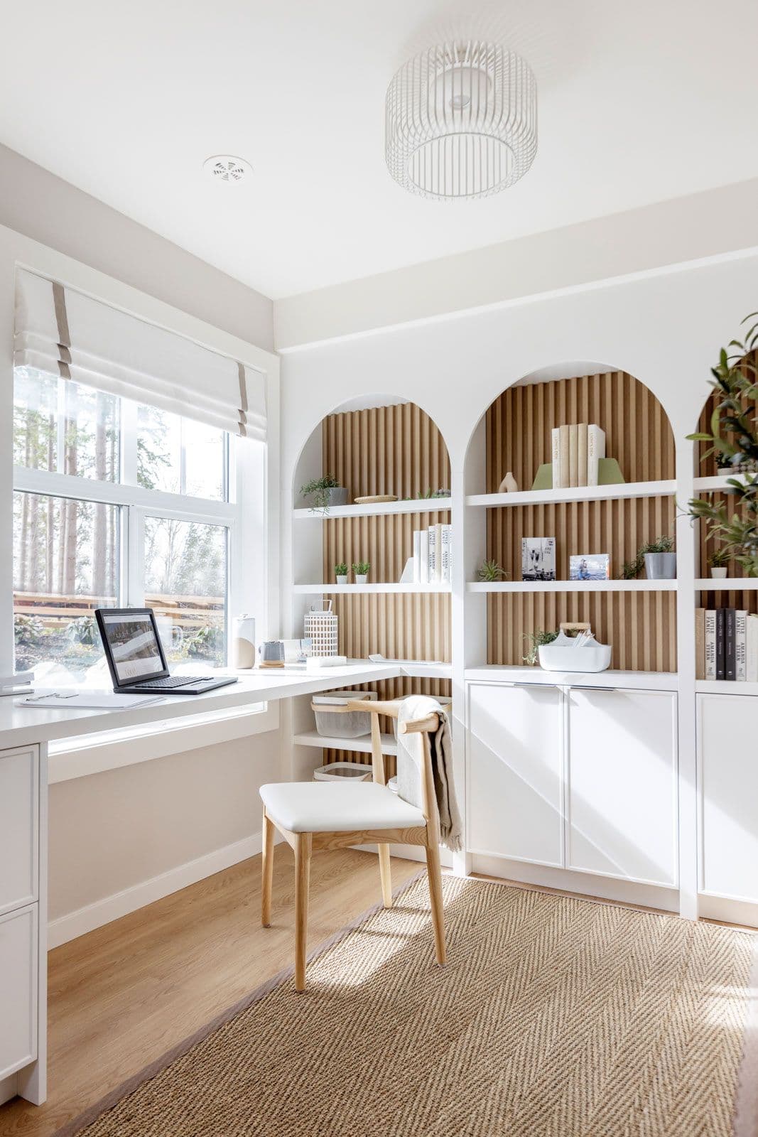 The Loop – Home office nook with a built-in desk, arched wood-slat shelving with books and decor, and a woven area rug.