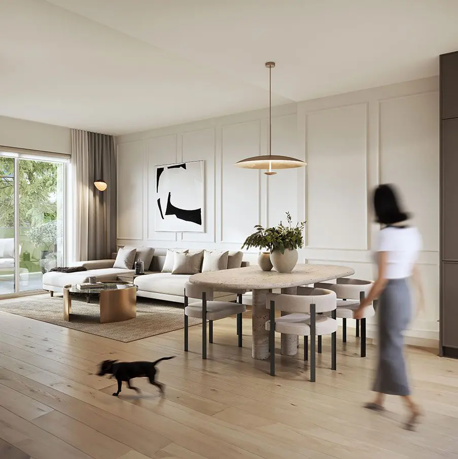 Morrison Walk – Living and dining area with a beige sectional sofa, a wood-and-marble oval dining table, black-and-white abstract art, and a small dog walking across the wood floor.