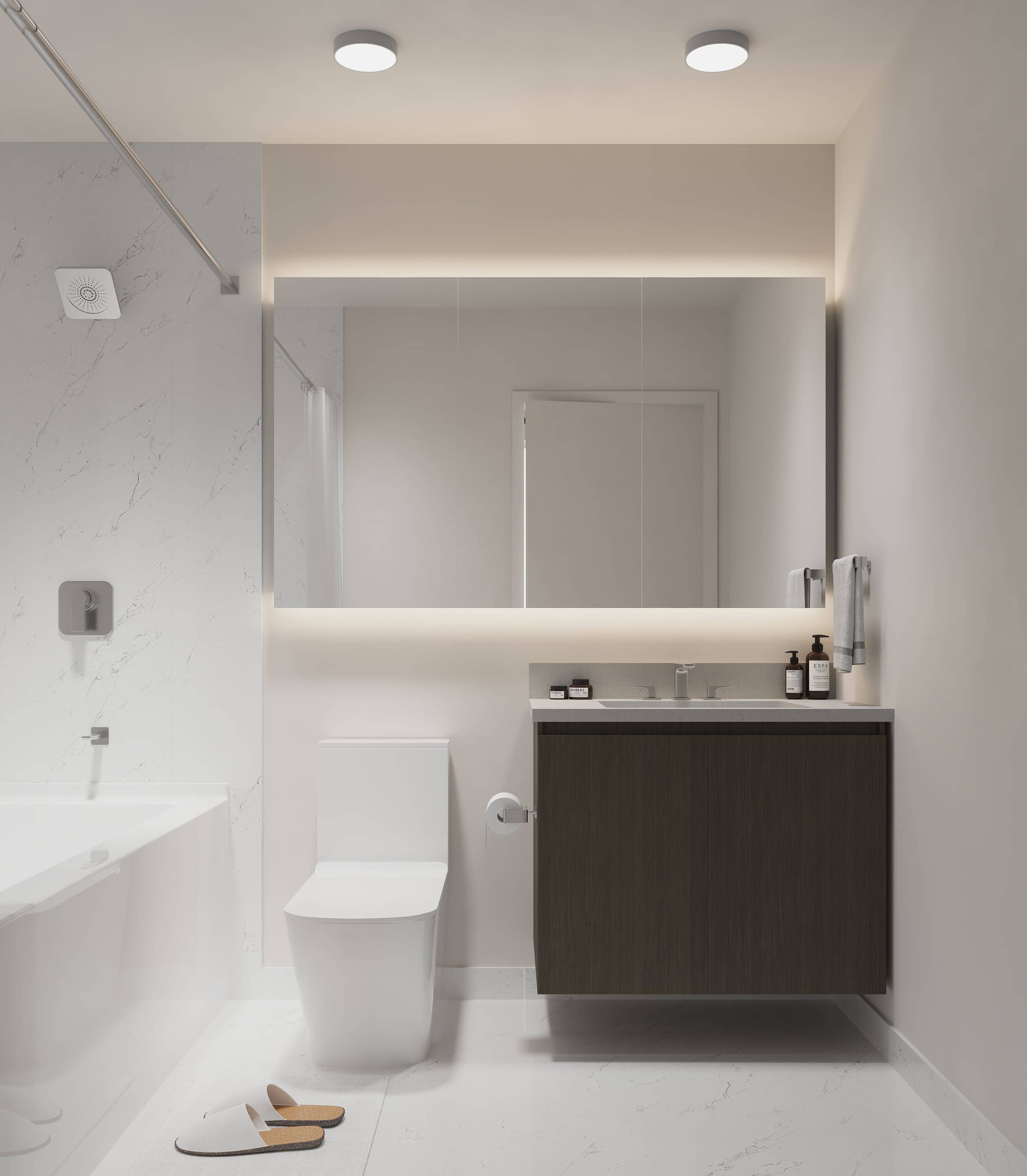 Terra Garden – A sleek, modern bathroom featuring a dark wood floating vanity, a backlit horizontal mirror, and a white toilet alongside a marble-tiled bathtub. The space is illuminated by soft integrated lighting and clean recessed ceiling fixtures for a bright, contemporary finish.