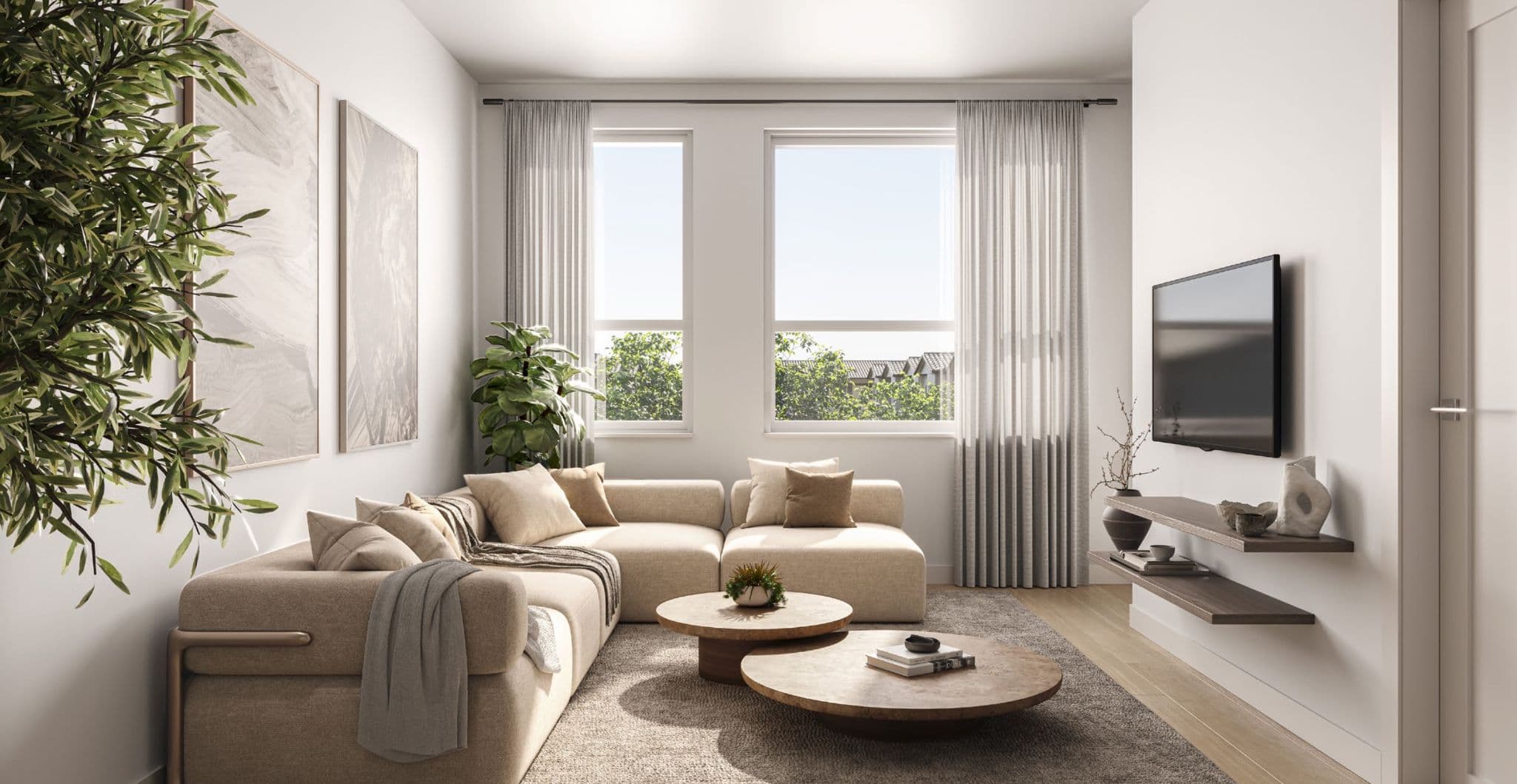 The Merchant – Living room with a beige sectional sofa, two round wood coffee tables, a wall-mounted TV, and a window looking out to trees and rooftops.