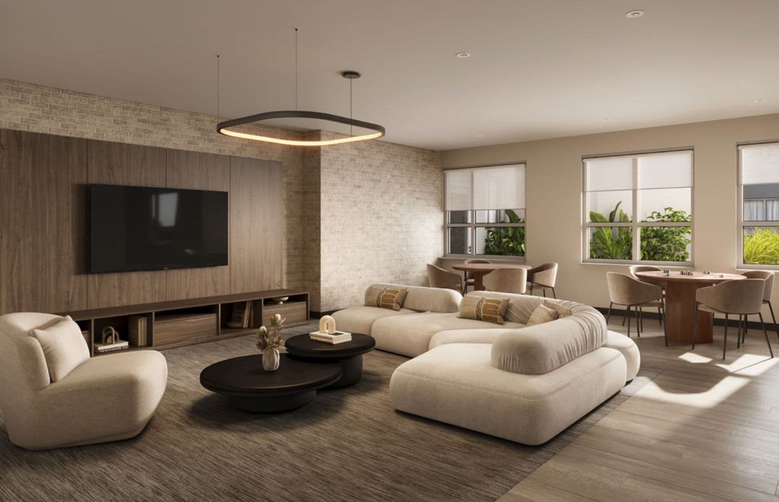 The Merchant – Shared lounge with a wall-mounted TV over wood millwork, a large curved sofa, an accent armchair, and a games/dining table by the windows.