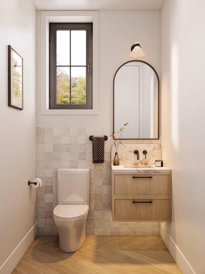 Wallace – A bright, compact powder room features light herringbone wood flooring, a white porcelain toilet, and an off-white square-tiled accent wall. A floating light-wood vanity with marble countertop and backsplash sits beneath an arched black-framed mirror, next to a black casement window overlooking lush green trees.