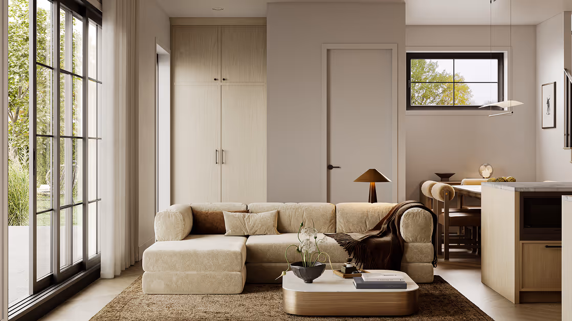 Wallace – A bright, open-concept living area featuring a plush cream sectional sofa, low coffee table, and tall floor-to-ceiling cabinetry set against warm neutral walls. Large black-framed glass sliding doors flood the room with natural daylight and look out onto lush outdoor greenery, while an adjoining dining table and kitchen island complete the space.