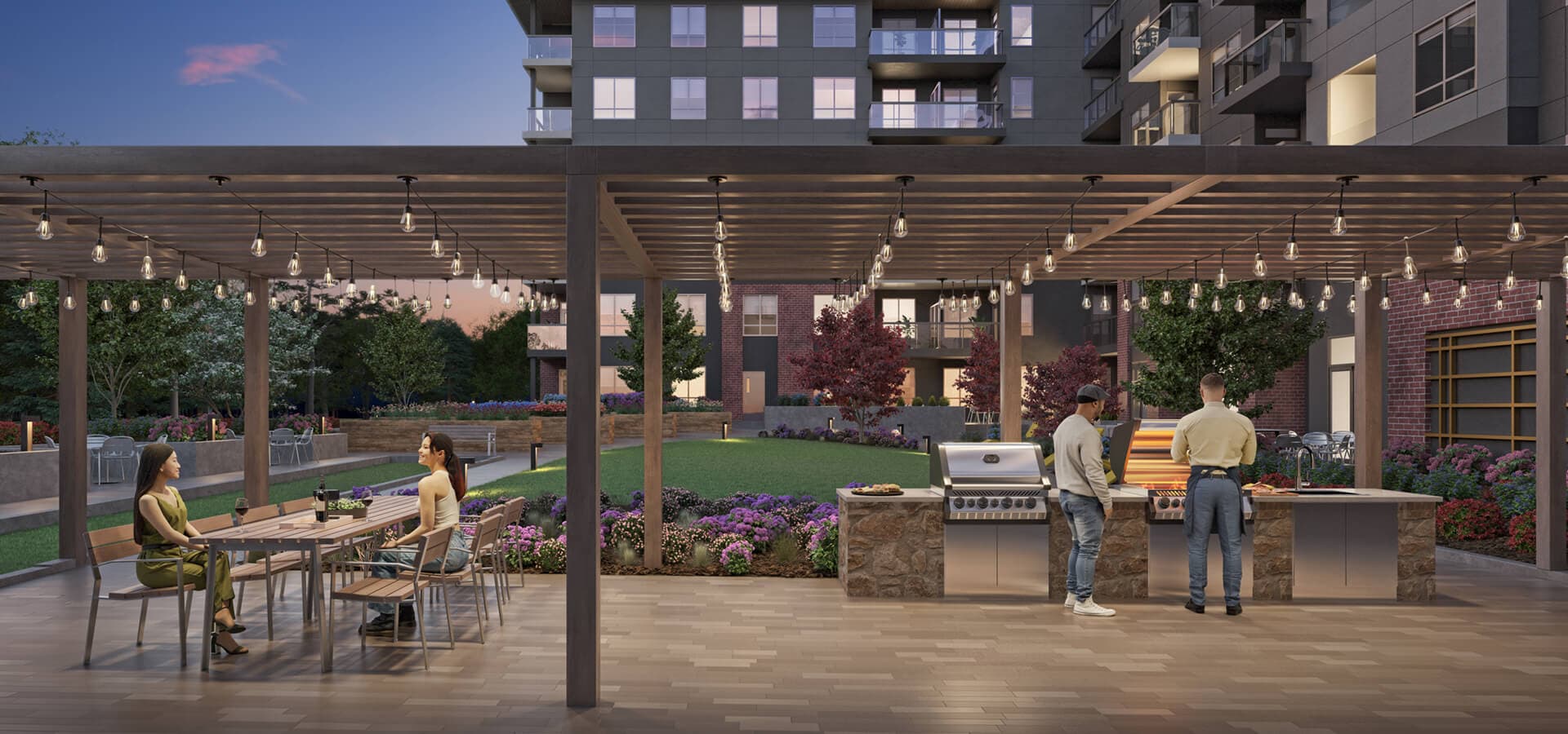 Guilden – An outdoor courtyard lounge at dusk under a pergola strung with string lights, with a communal dining table, an outdoor BBQ kitchen area, landscaped flower beds, and residential buildings around it.