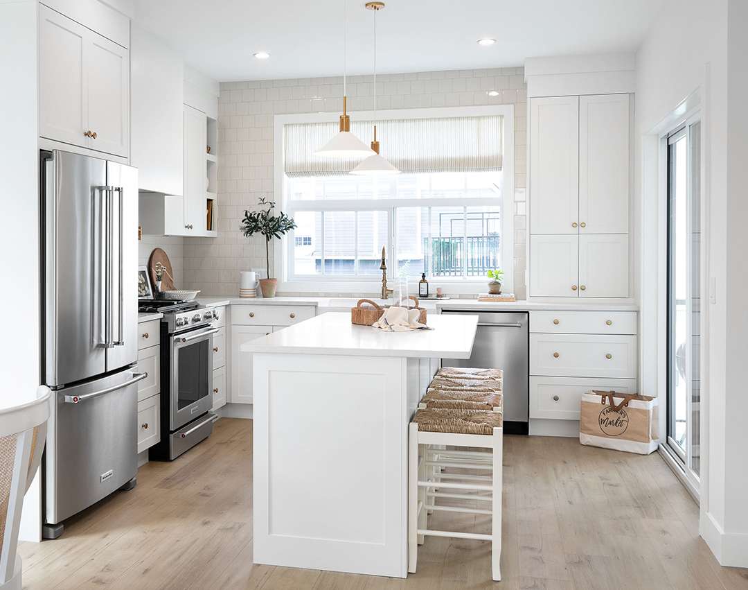Renfrew South – White kitchen with stainless steel fridge and range, a central island with bar stools, and a sliding glass door leading to a balcony.