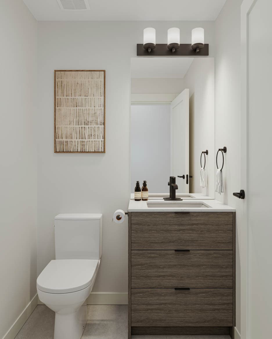 Kin & Kith – Powder room featuring dark wood vanity with three drawers, rectangular mirror, three-bulb sconce lighting, toilet, and artwork.