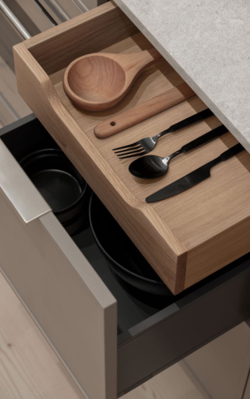 Naímo – Close-up of an open kitchen drawer with a wooden utensil organizer holding a serving spoon, spatula, fork, spoon and knife, with pots stored below.