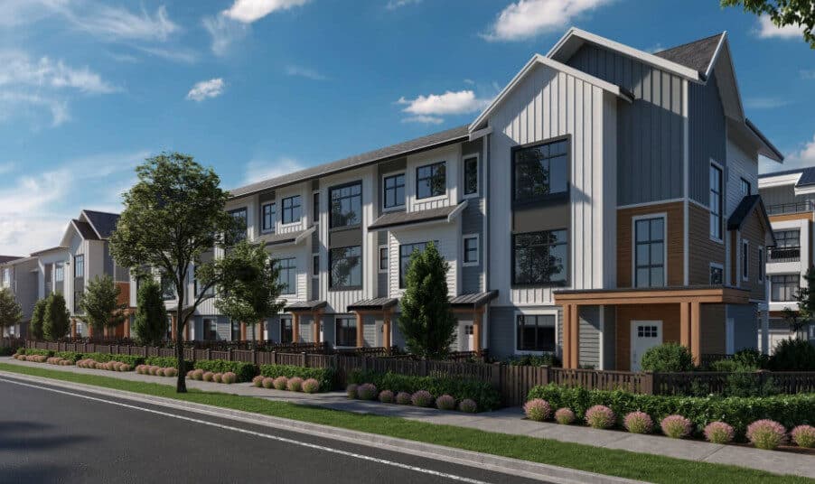 Aviva – A street-level shot displays modern three-story townhomes with white vertical paneling, dark grey siding, and natural wood accents over the entrances. The buildings feature landscaped front yards with dark wooden fencing, green bushes, and young trees under a clear blue sky.