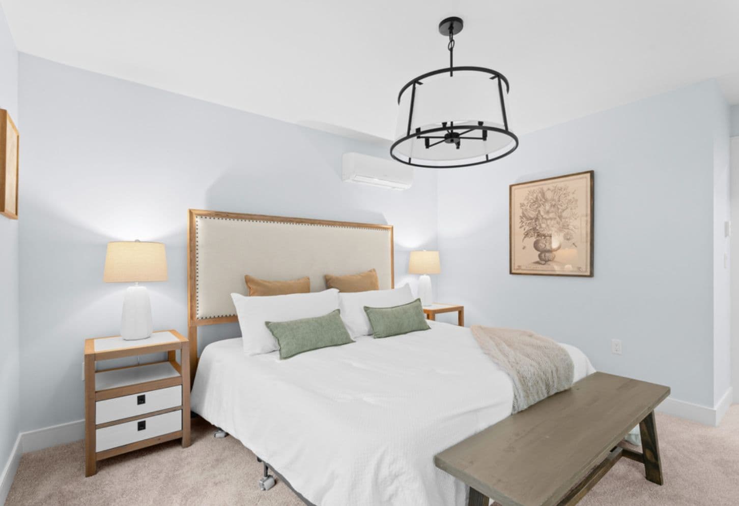 Raven's Park – Bedroom with a white-bedded bed, upholstered headboard, matching wood nightstands with lamps, a wood bench at the foot of the bed, and a black drum pendant light.
