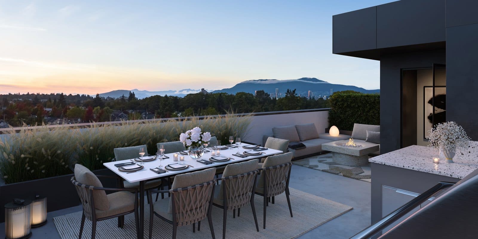 King and Columbia – A modern rooftop patio features an eight-seat dining table set with fine dinnerware alongside a cozy lounge area with an outdoor fire pit. The space overlooks a vast landscape of lush treetops, distant city buildings, and mountain peaks under a soft twilight sky.