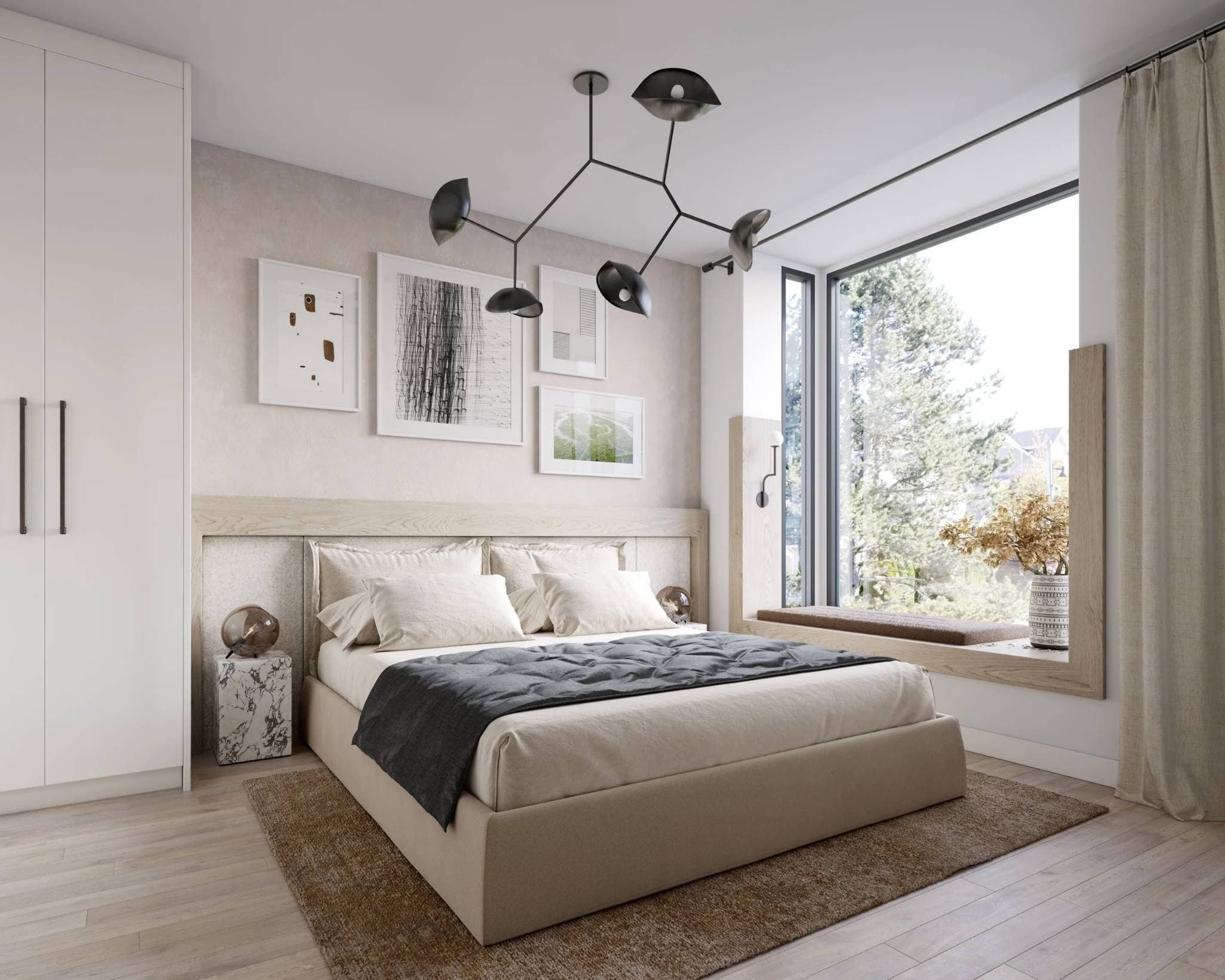 King and Columbia – A modern bedroom feature a low-profile upholstered bed with light beige linens, a black modern branch chandelier, and a wood-framed window bench overlooking lush green trees. Light wood floors, neutral gallery artwork above the headboard, and marble nightstands create a serene and stylish atmosphere bathed in daylight.