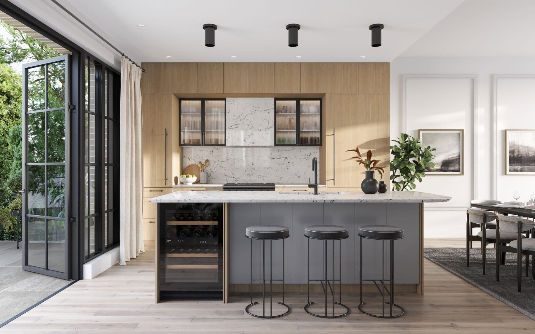 King and Columbia – A modern open-concept kitchen featuring light wood millwork, a white marble backsplash, and a grey island equipped with an integrated wine fridge and three black barstools. Black metal-framed glass doors fold open onto a sunlit patio surrounded by lush green trees.
