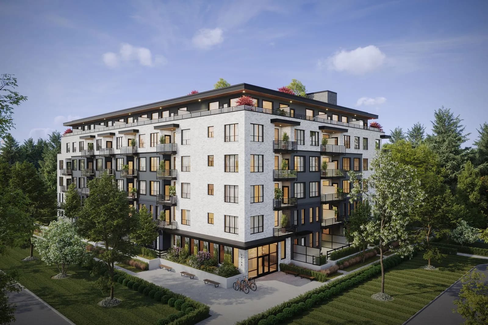 Guildford The Greatest 2 – An elevated corner render of a modern six-story residential building featuring a textured white brick and dark charcoal facade with private balconies and a landscaped rooftop terrace. The property is surrounded by manicured green lawns, trees, perimeter hedging, and a paved walkway with benches and bike racks under a clear blue sky.