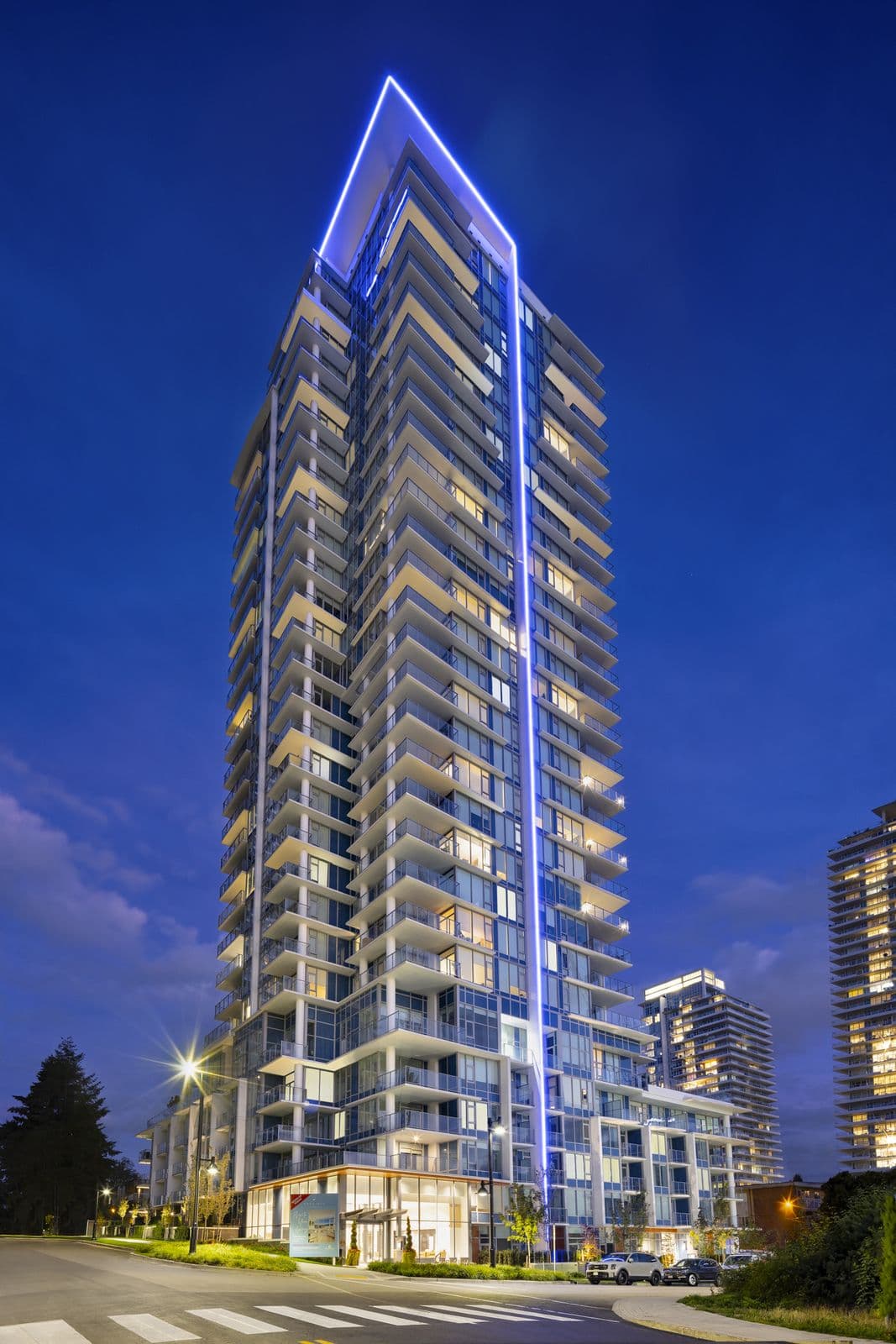 Precidia – Twilight photo of the tower illuminated with a blue LED accent light outlining its crown, other high-rises visible nearby.