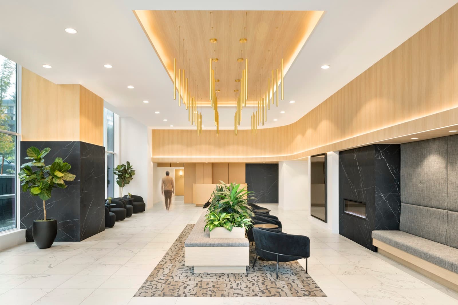 Precidia – Grand building lobby lounge with a cascading gold tubular light fixture, black marble accent walls, a fireplace, and seating.