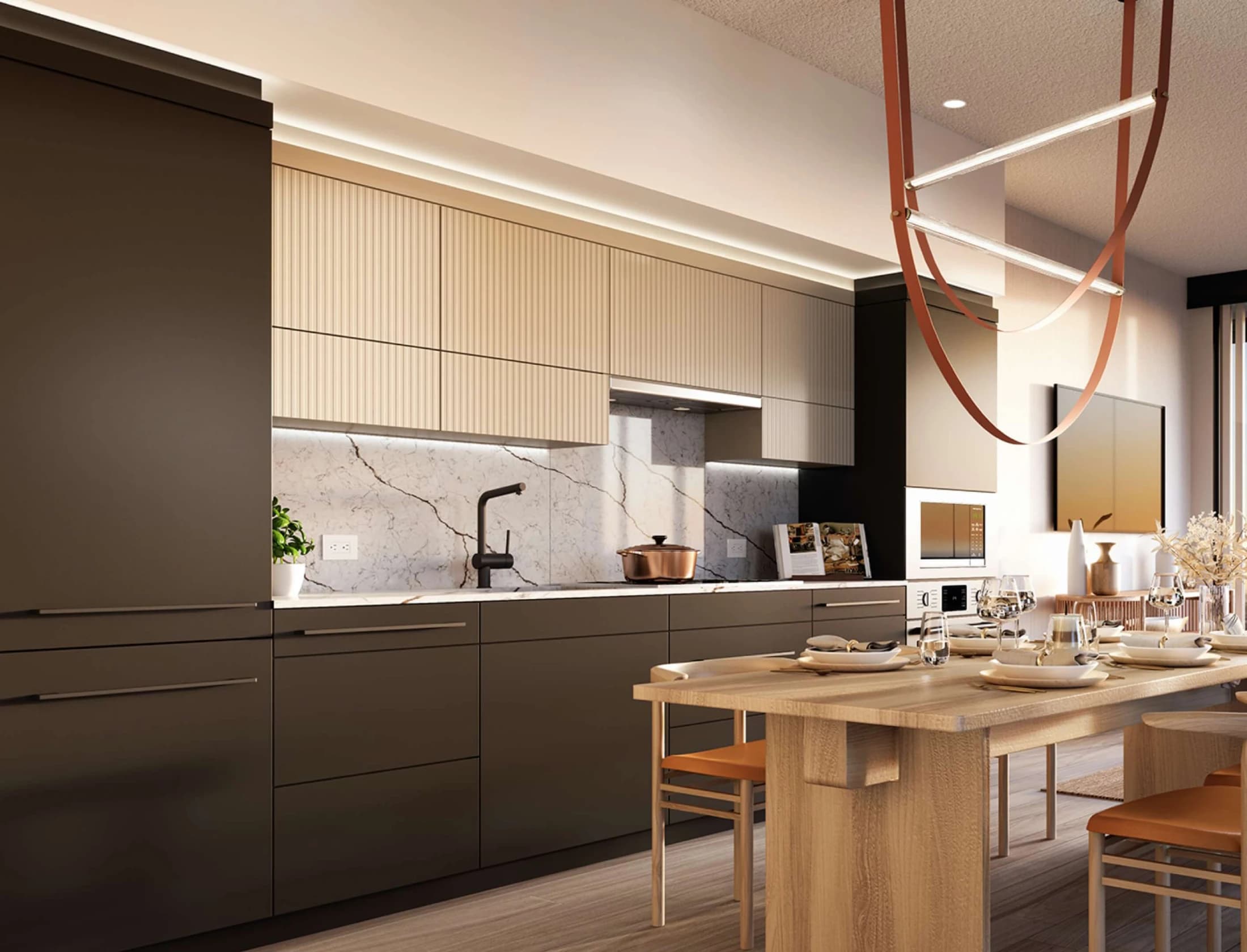 Concord Metrotown – A modern residential kitchen features two-tone cabinetry with dark matte lower cabinets, ribbed beige upper cabinets, and a white marble backsplash with under-cabinet lighting. Adjacent to the counter is a light wood dining table set for a meal, illuminated by an oversized, terracotta-colored sculptural light fixture hanging overhead.