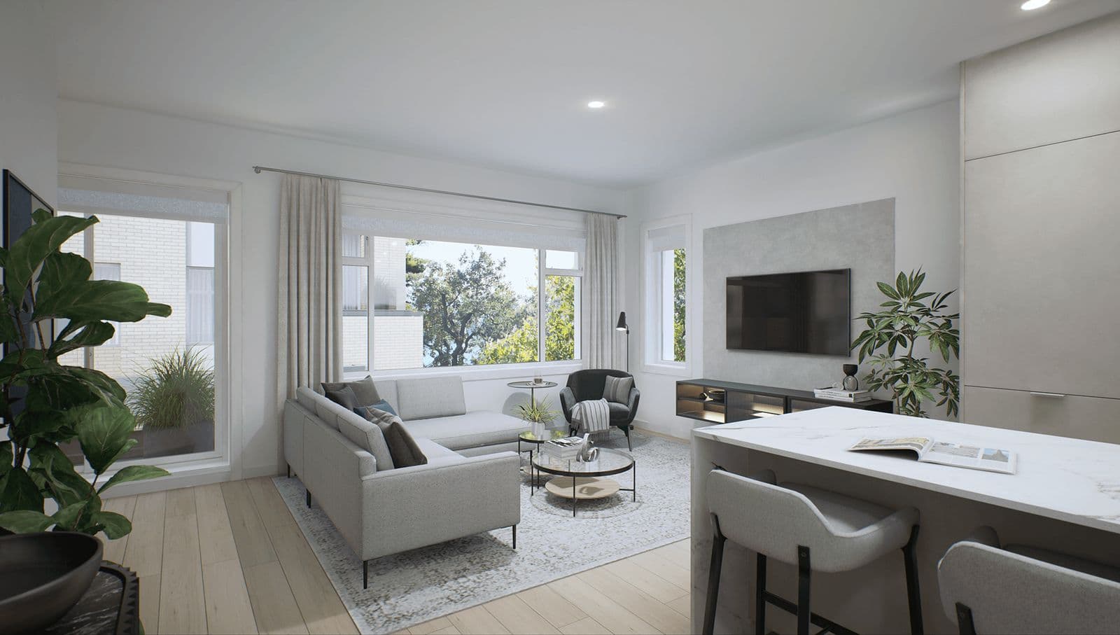 Terza – Living room with a gray sectional sofa, TV, and a kitchen island visible beyond, with large windows showing trees outside.