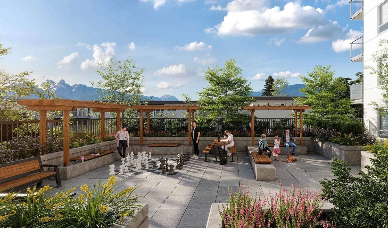 Thomas West Haney – A sunny outdoor rooftop courtyard featuring wooden pergolas, bench seating, picnic tables, and a giant floor chess set where people are socializing. Lush planter boxes surround the paved patio, offering scenic views of distant mountain peaks under a bright sky.