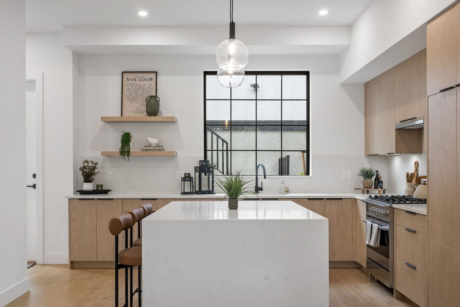 Archer at Latimer – Kitchen with light wood cabinets, white countertops, built-in shelving, and a window looking onto an exterior stairwell.