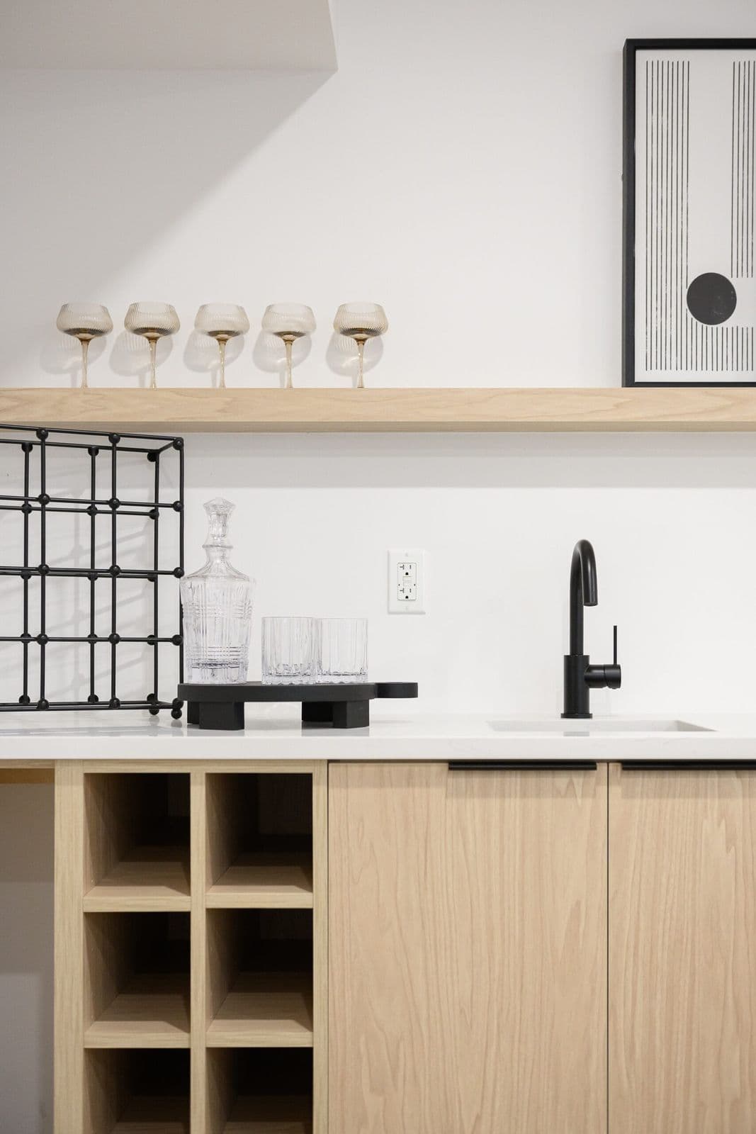 Archer at Latimer – Close-up of a wet bar counter with a wine rack, crystal decanter and glasses, black faucet, and framed artwork above.