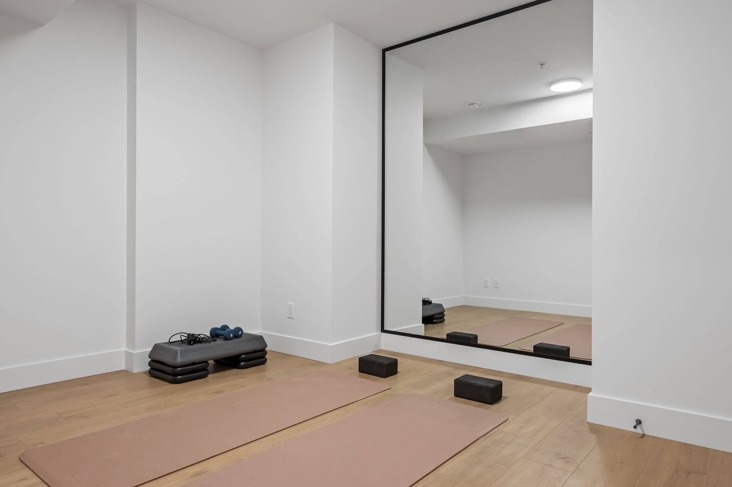 Archer at Latimer – Basement flex room set up as a home gym, with a large mirror, yoga mats, dumbbells, and a step platform.