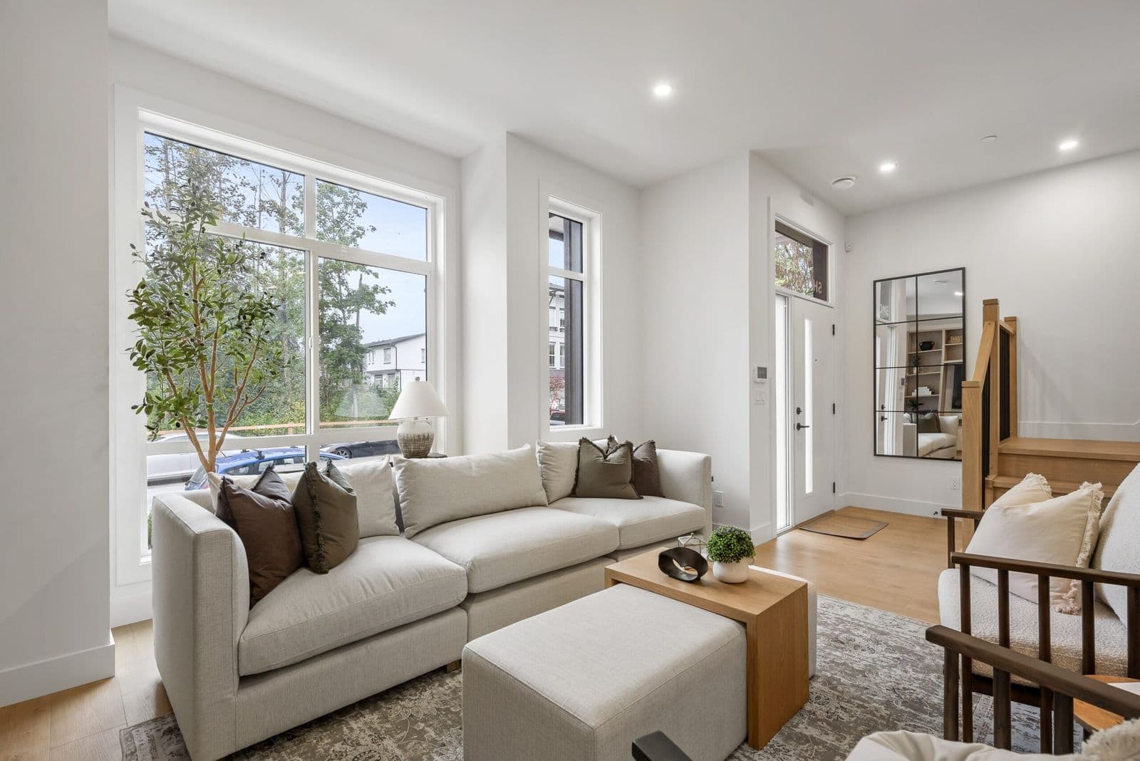 Archer at Latimer – Living room with light sofa and armchairs, floor-to-ceiling windows overlooking the street, and a mirror and staircase in the background.