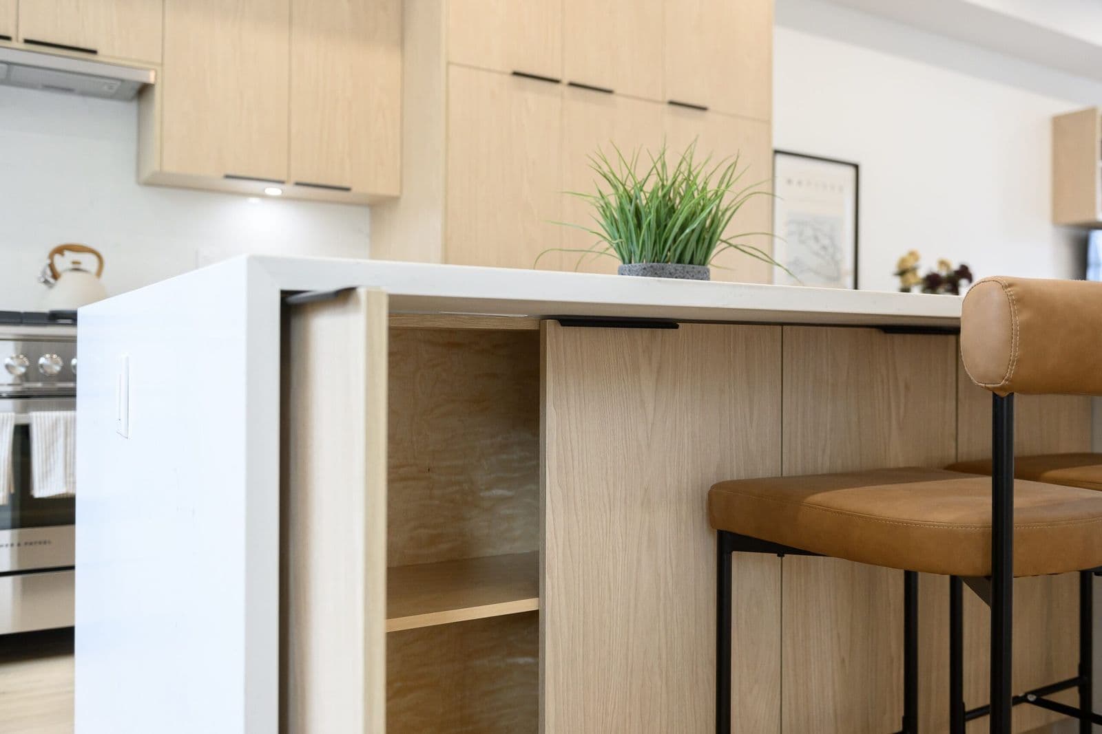 Archer at Latimer – Close-up of a kitchen island with an open cabinet, potted plant, and leather-topped bar stool.