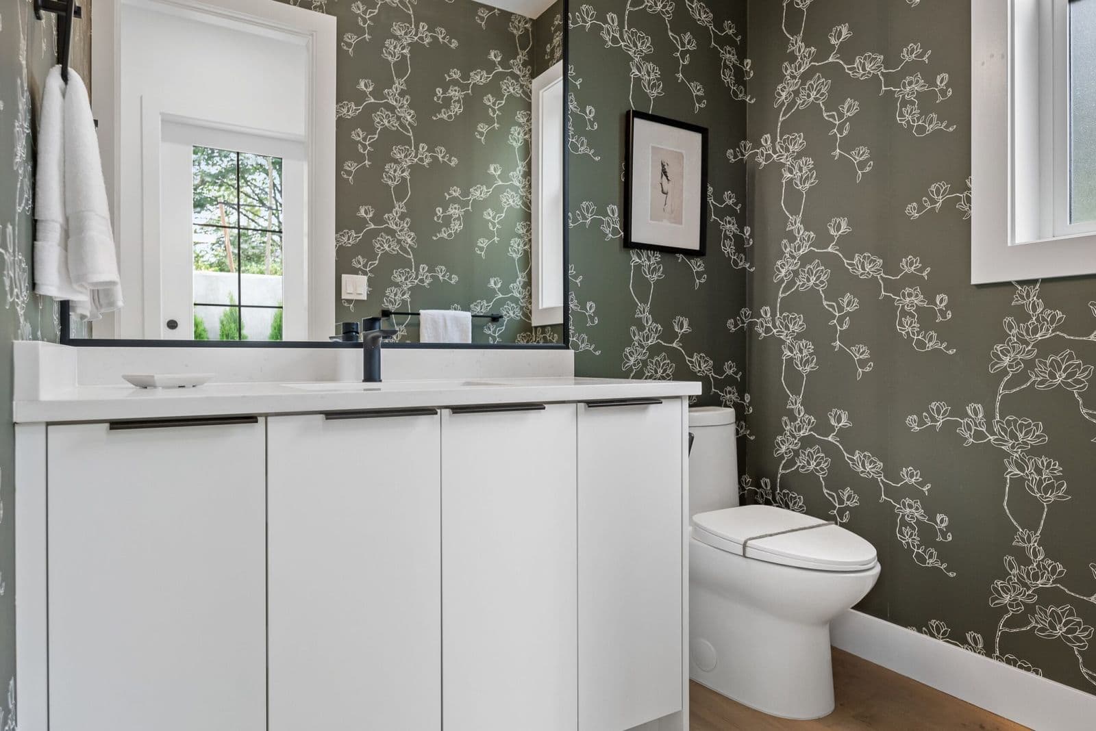 Archer at Latimer – Powder room with dark floral wallpaper, white floating vanity, black fixtures, and a framed sketch on the wall.
