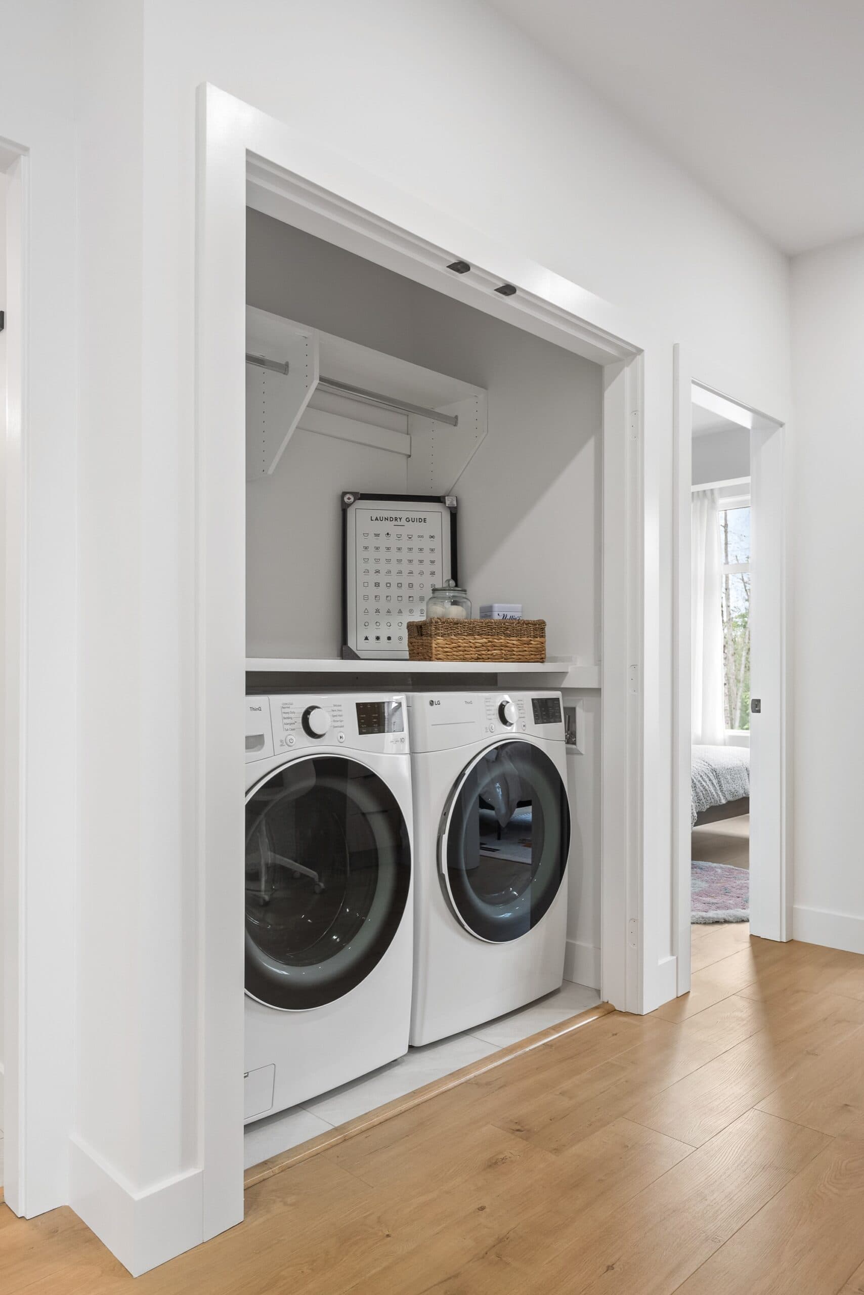 Archer at Latimer – Laundry closet with a stacked white front-load washer and dryer, a laundry guide poster, and a shelf with a basket above.