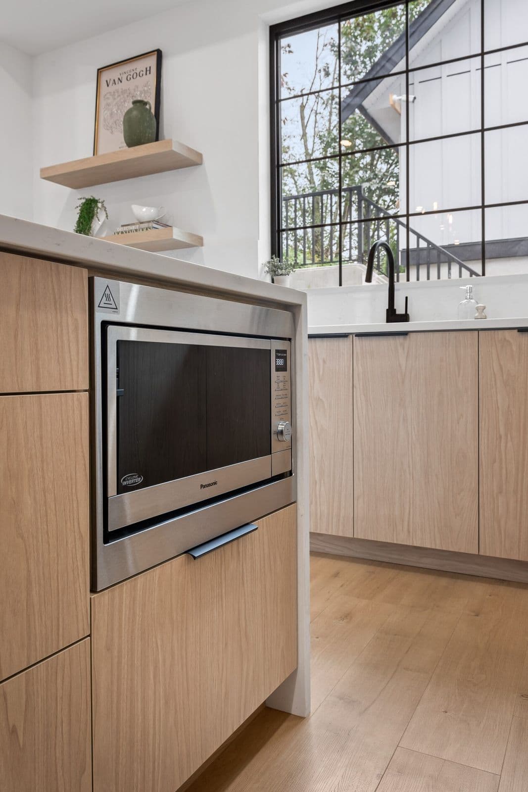 Archer at Latimer – Kitchen corner with built-in microwave, wood cabinetry, and a tall window looking onto an exterior stairwell and courtyard.